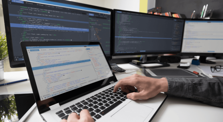 Persona frente a un computador y múltiples pantallas revisando códigos de programación