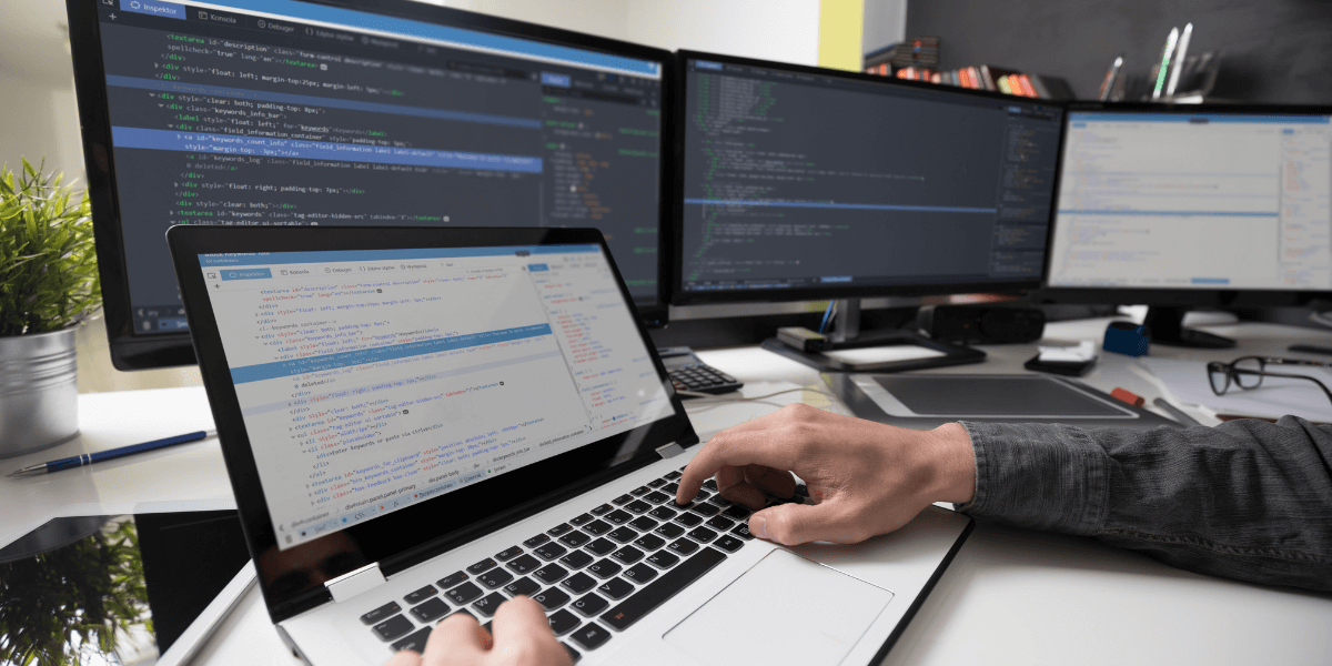 Persona frente a un computador y múltiples pantallas revisando códigos de programación